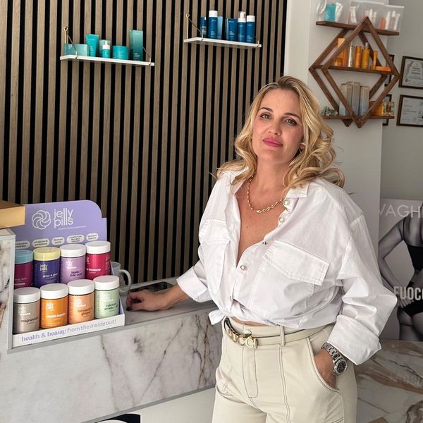 Una mujer con camisa blanca y pantalones caqui se apoya en un mostrador de una tienda de belleza, rodeada de productos.