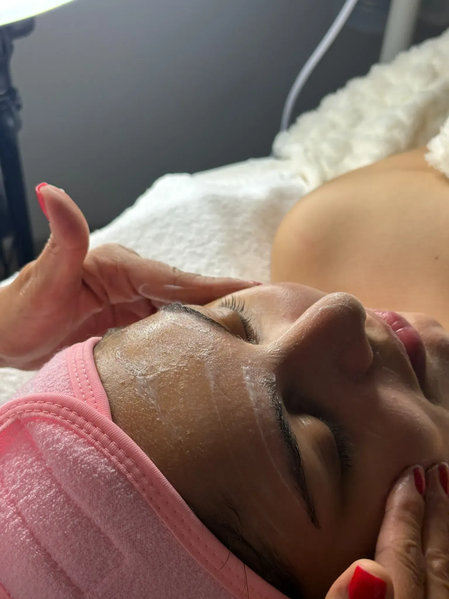 Una mujer está recibiendo un tratamiento facial con una toalla rosa en la cabeza.