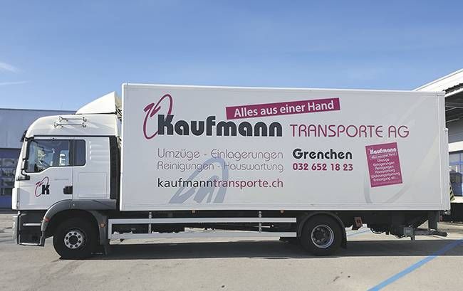 Weisser LKW mit Logo und Schriftzug „Kaufmann Transporte AG“; geparkt im Freien an einem sonnigen Tag.
