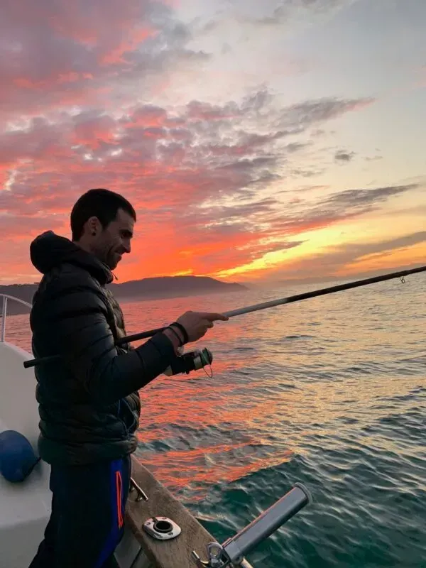 Un hombre está pescando en un barco al atardecer.