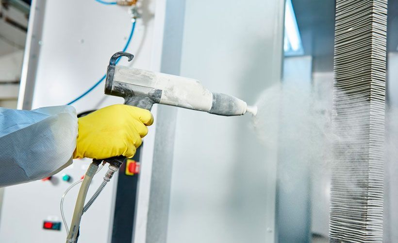 Un trabajador con guantes amarillos pinta con aerosol una superficie metálica en un taller industrial.