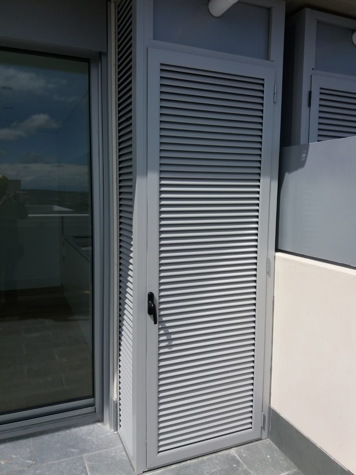 Armario de balcón blanco con persianas junto a una puerta corredera de cristal en un patio soleado.