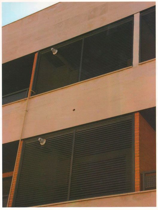 Exterior de un edificio moderno con paredes color canela, ventanas oscuras con celosías y pequeñas luces bajo los aleros.