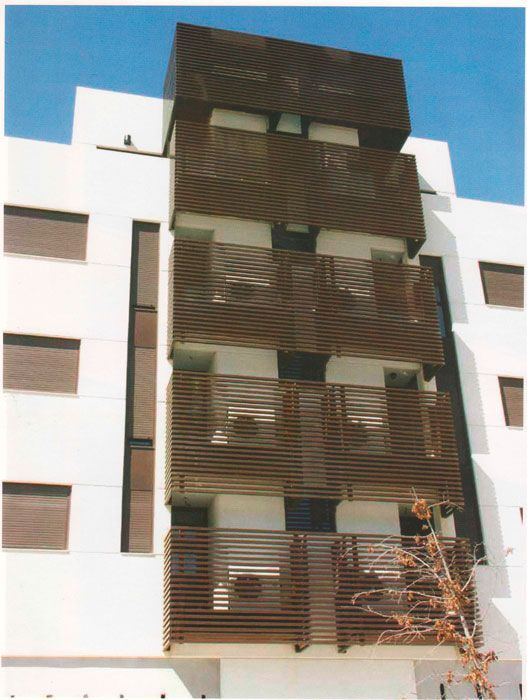 Edificio de apartamentos moderno con paredes blancas y balcones con toldos marrones contra un cielo azul.
