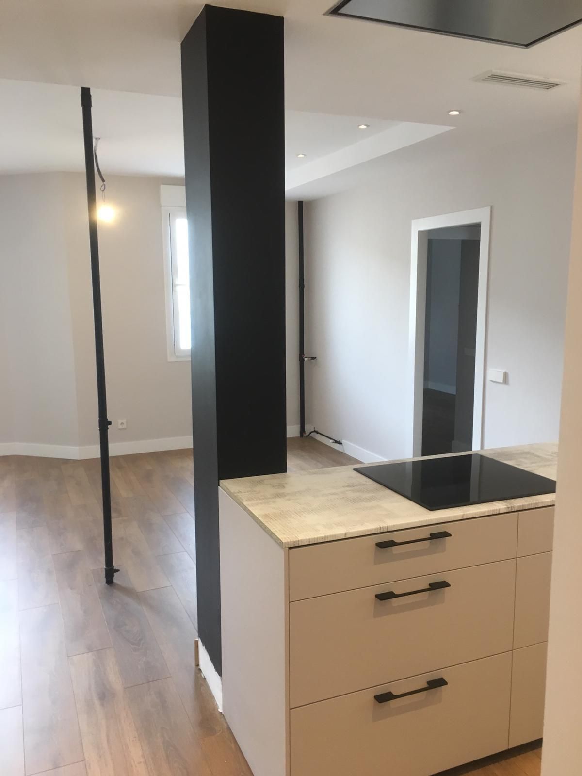 Cocina moderna con isla, campana extractora negra, armarios blancos y suelo de madera noble que da a una puerta.