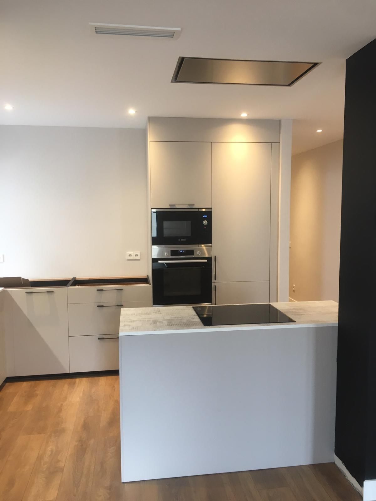 Cocina moderna con gabinetes blancos, horno empotrado, isla de mármol, piso de madera y pared decorativa negra.