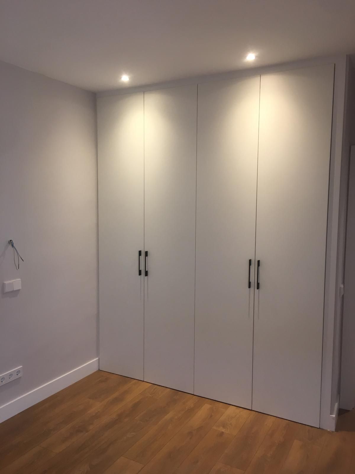 Armario vacío de dormitorio blanco con tres puertas, paredes grises y suelo de madera.