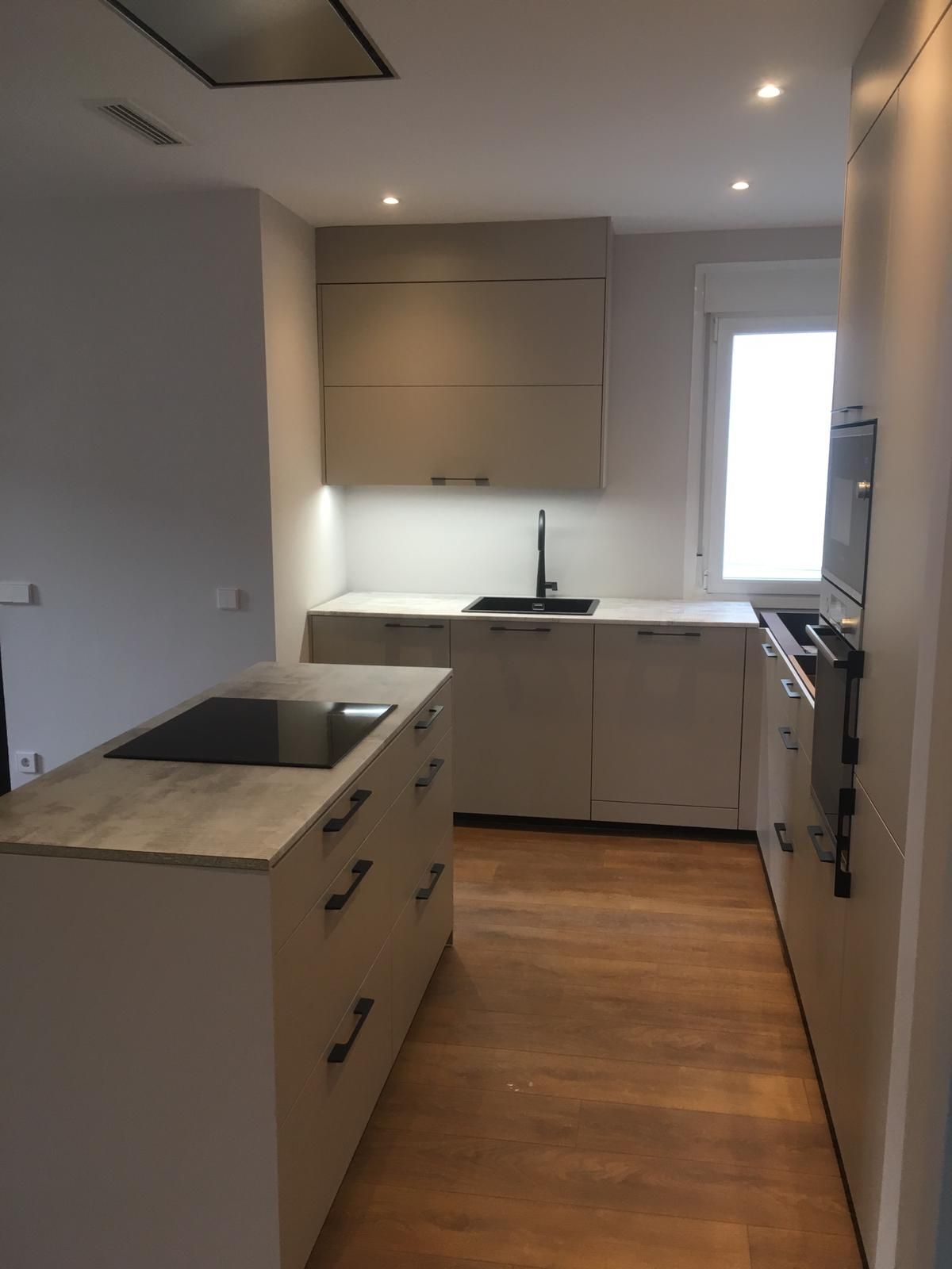 Cocina moderna con gabinetes beige, piso de madera, encimera negra y electrodomésticos de acero inoxidable.