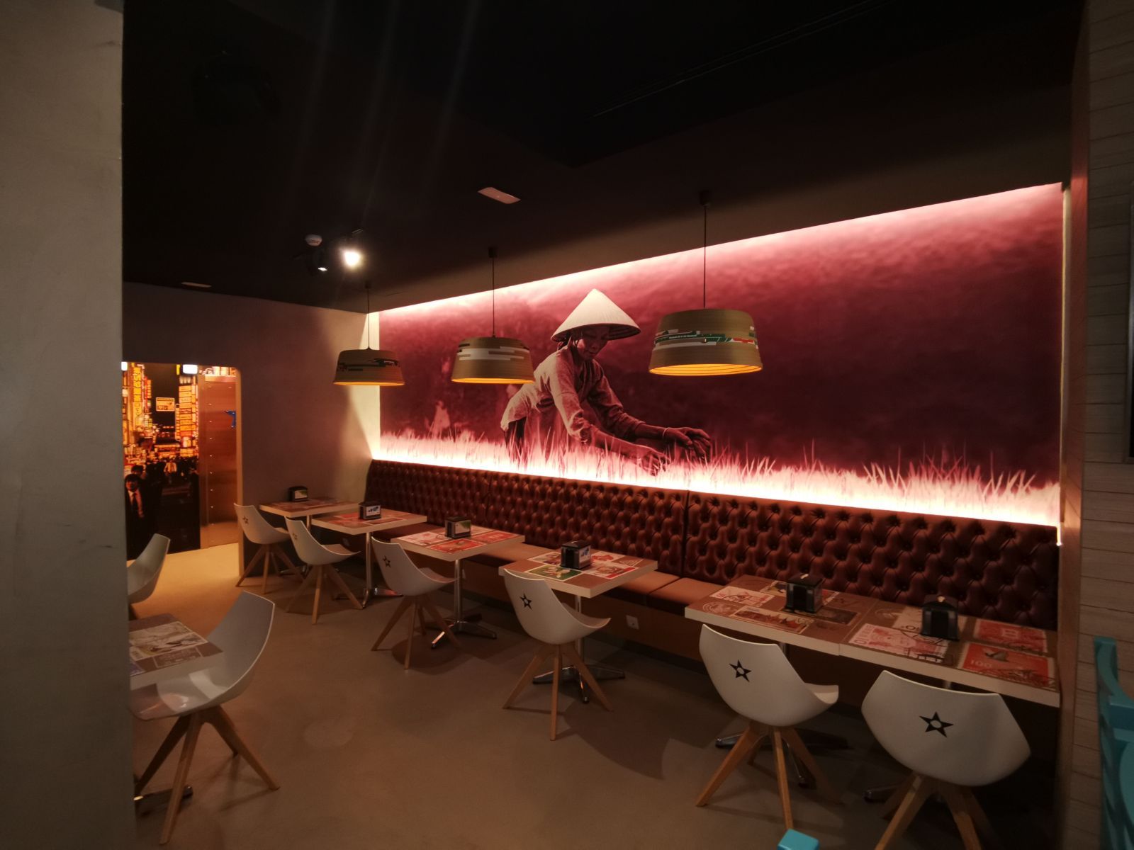 Interior elegante del restaurante con iluminación de neón rosa, pared mural y mesas y sillas vacías.