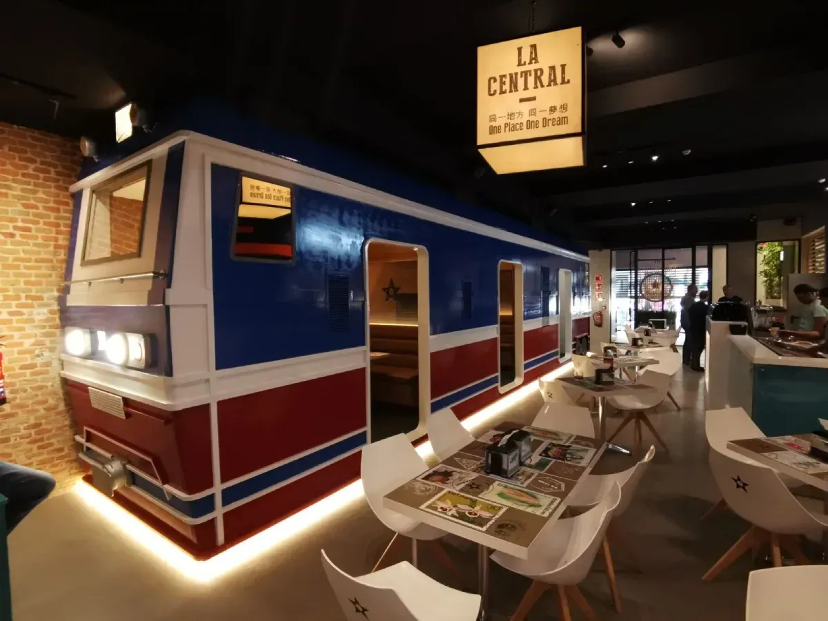 Comedor tipo vagón de tren azul y rojo en un restaurante con mesas y sillas.