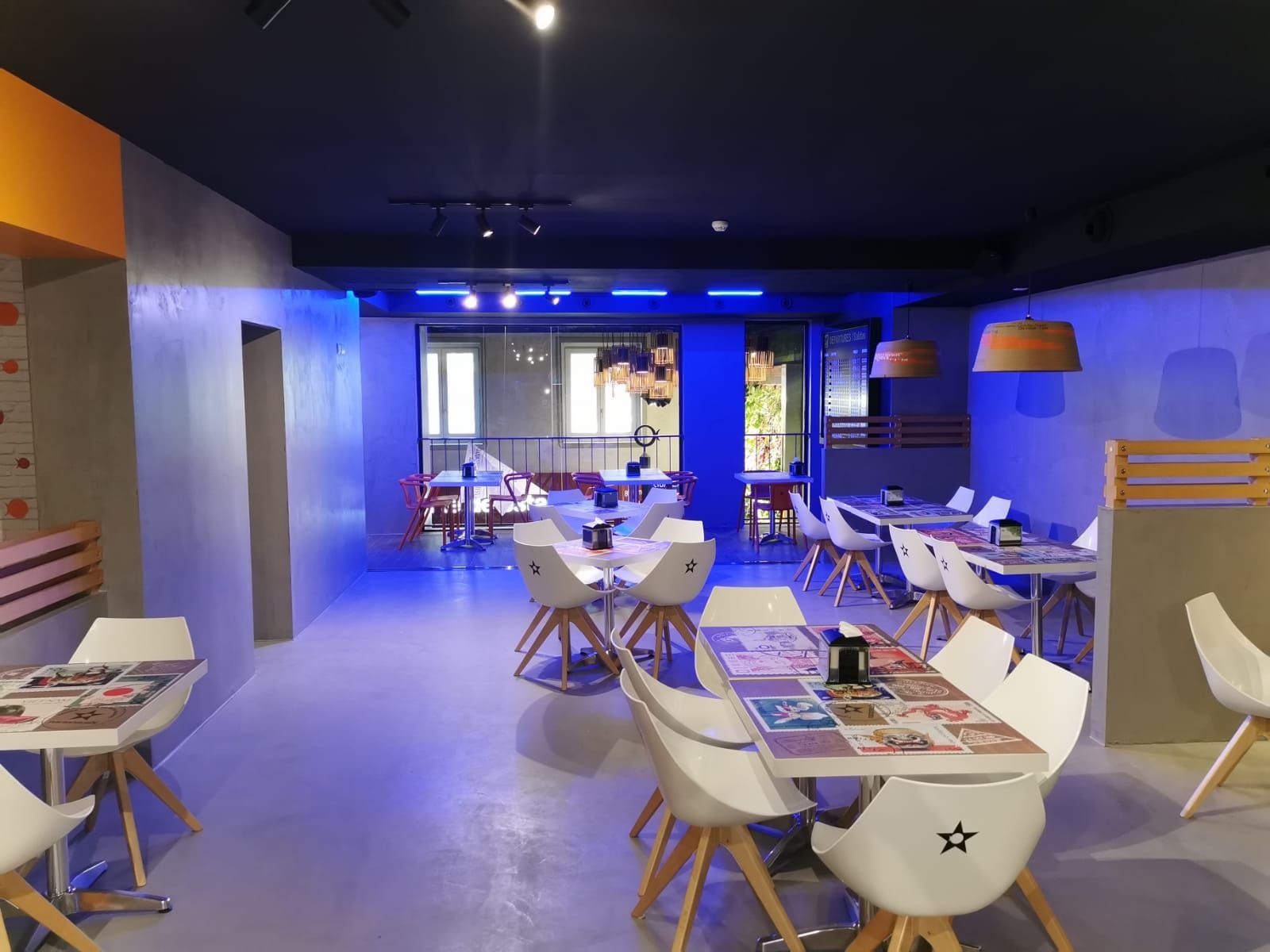 Interior de cafetería moderno con sillas blancas, mesas de madera, iluminación azul