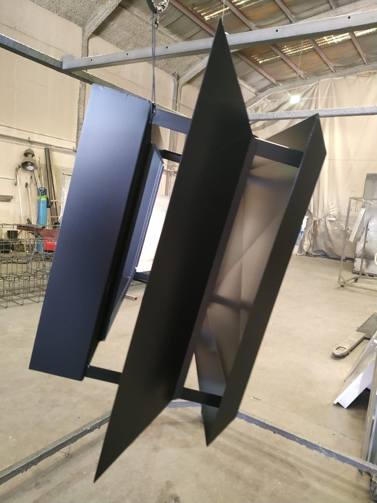 Escultura geométrica abstracta en negro y azul que cuelga en un taller o estudio.