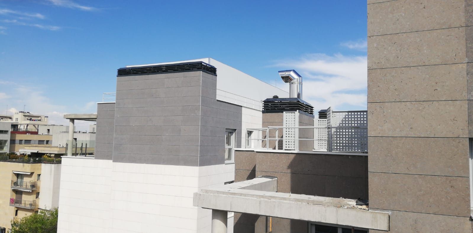 Vista desde la azotea de edificios blancos y grises bajo un cielo azul.