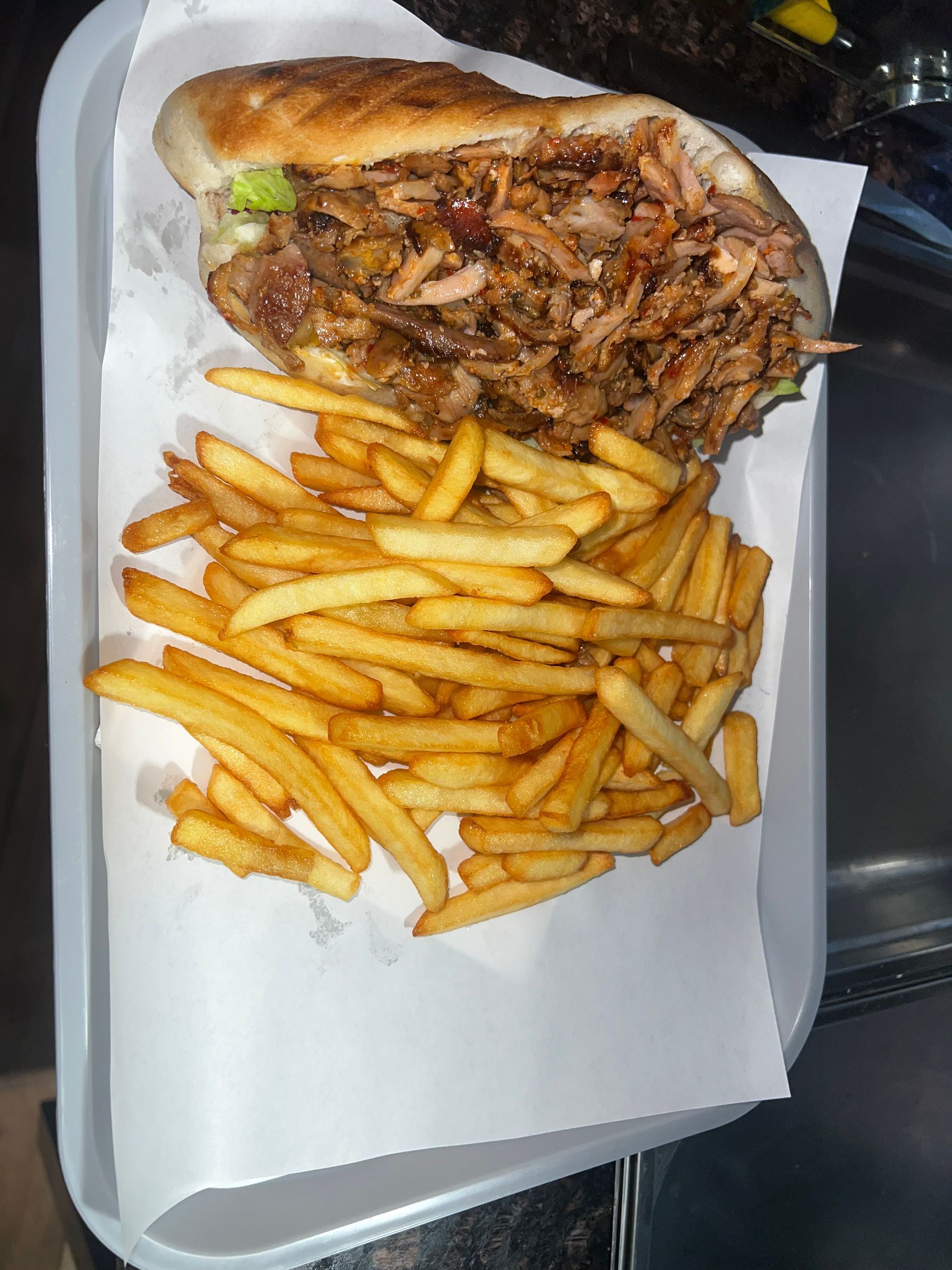 Un sandwich copieux garni de viande effilochée et accompagné de frites dorées, le tout servi sur un plateau blanc recouvert de papier.