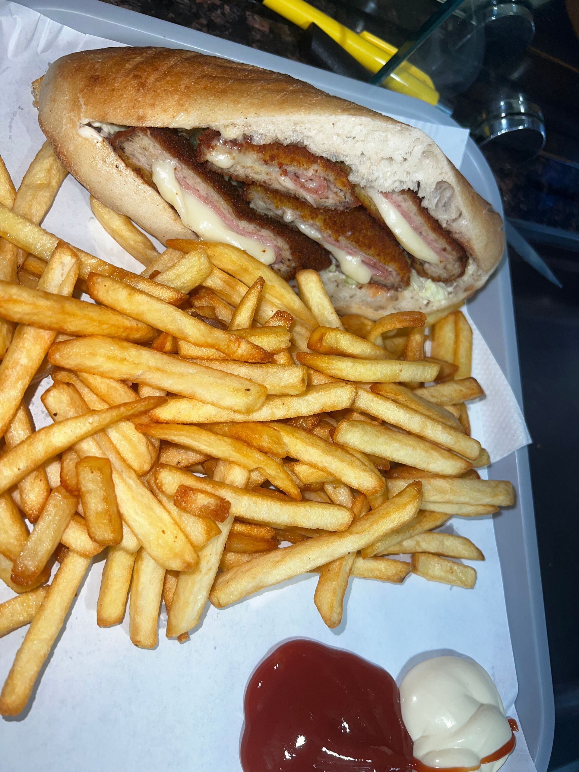Un sandwich à la viande et au fromage, servi avec une montagne de frites dorées et des touches de ketchup et de mayonnaise.