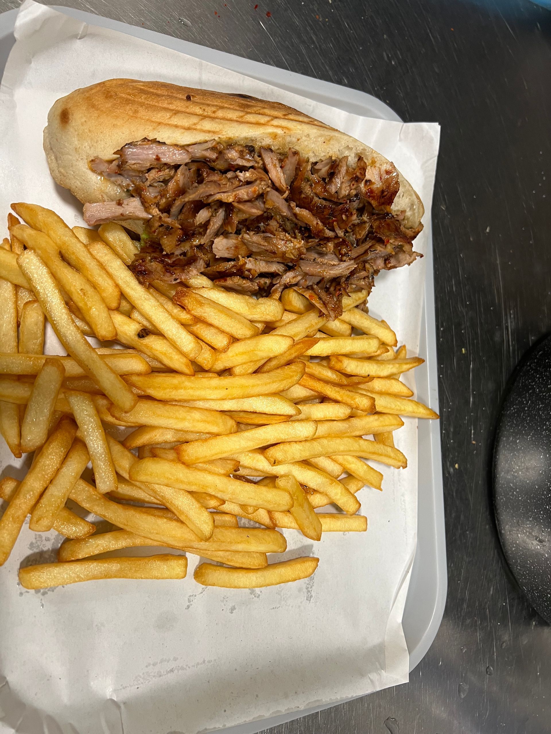 Un sandwich grillé garni de viande effilochée, servi avec une généreuse portion de frites dorées sur un plateau.