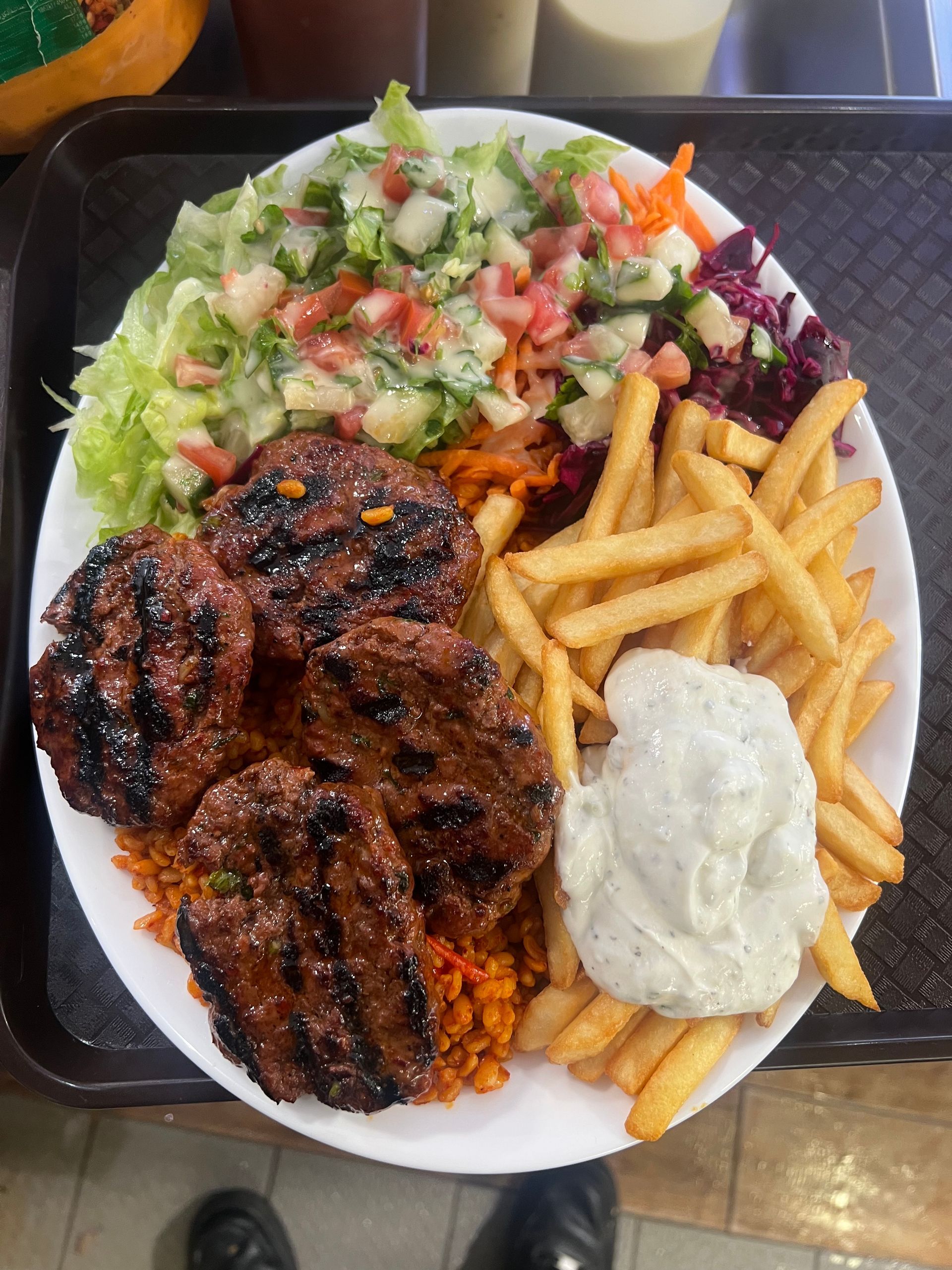 Une assiette de galettes de viande grillées, de frites, de salade et d'une cuillerée de sauce blanche, servie sur un plateau.