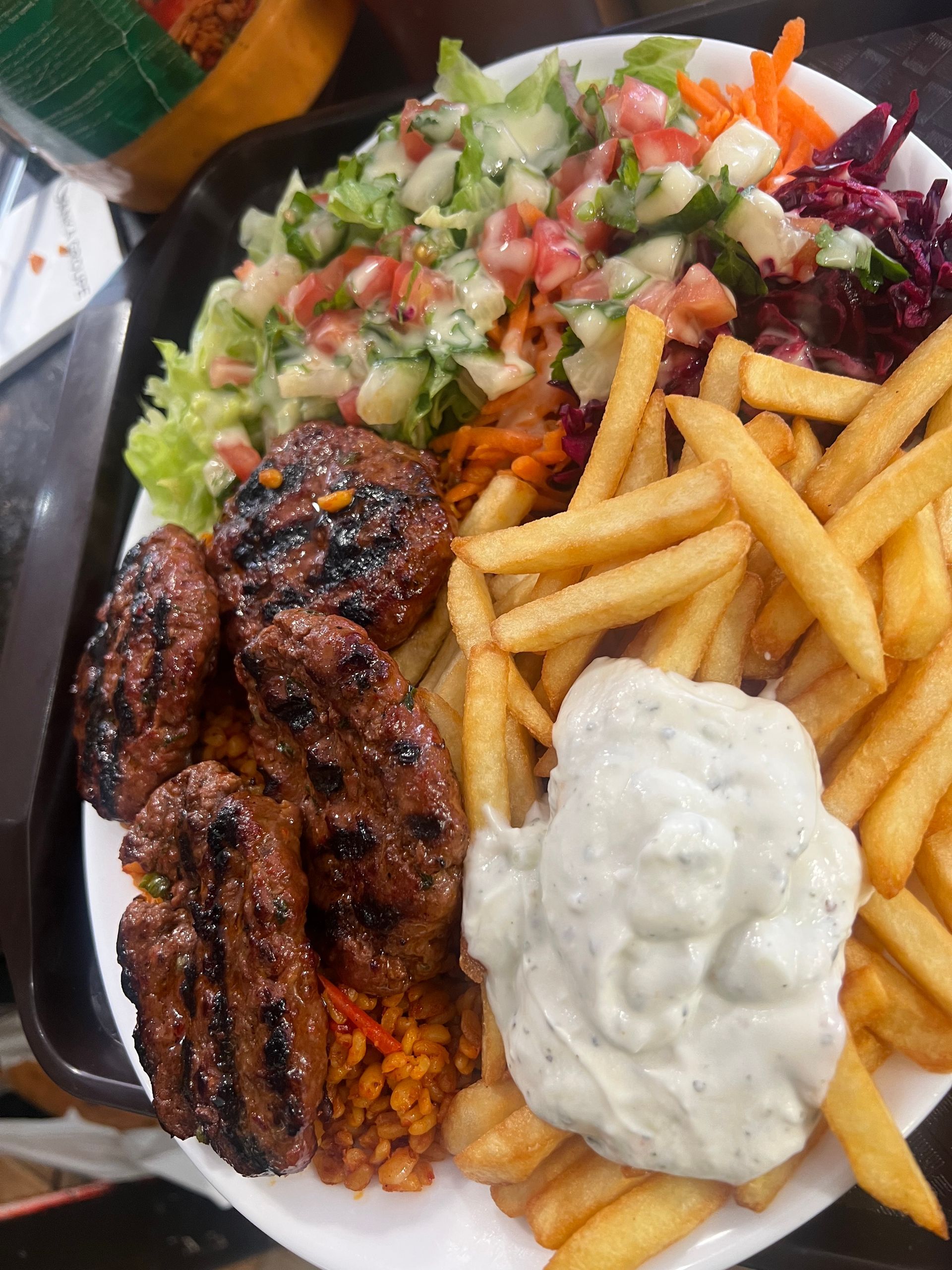 Une assiette de kefta grillée, des frites, une salade d'accompagnement, du chou rouge et une généreuse cuillerée de sauce tzatziki.