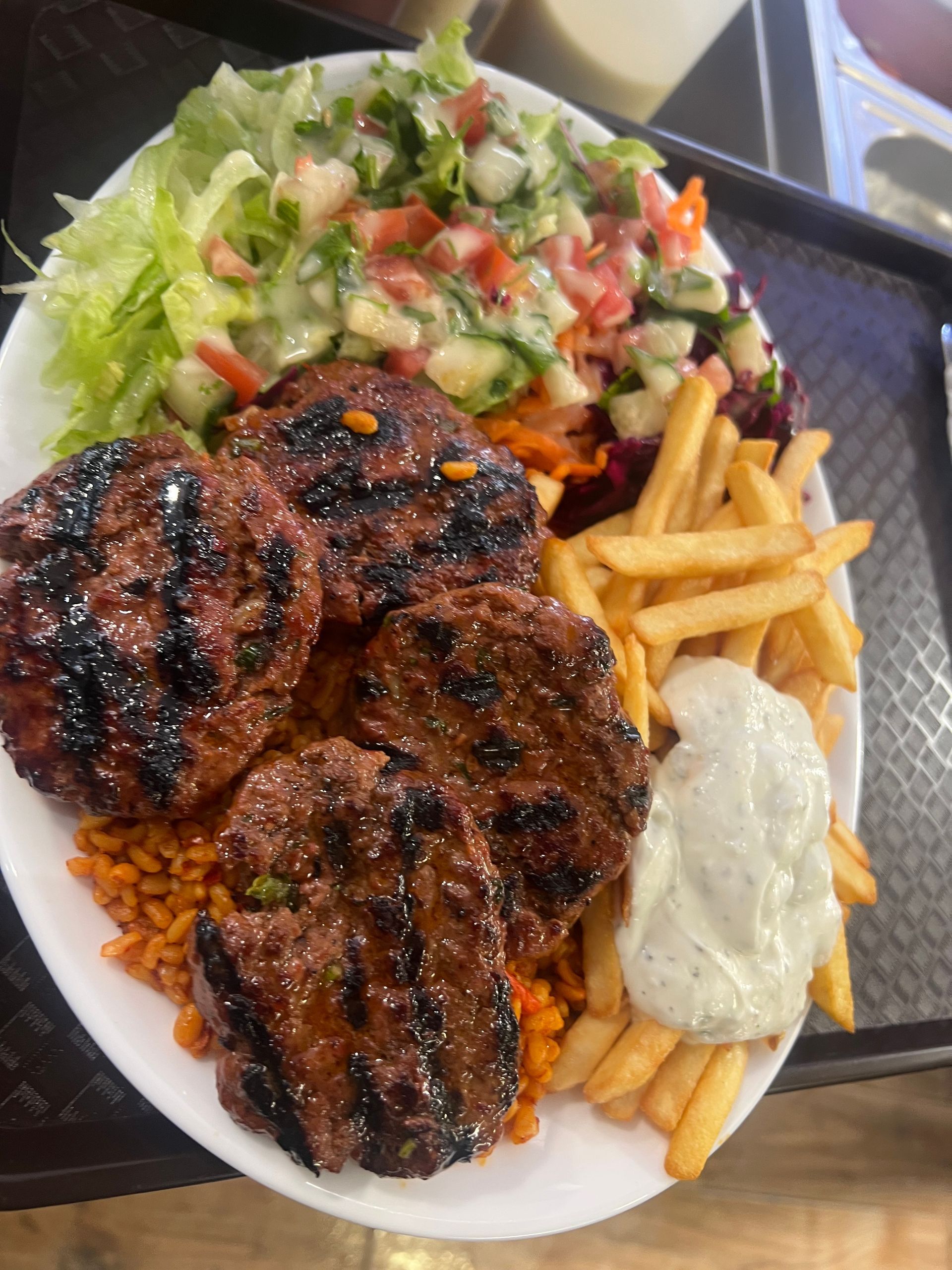 Une assiette composée de galettes grillées, de frites, d'une salade verte fraîche, de riz assaisonné et d'une cuillerée de sauce blanche.