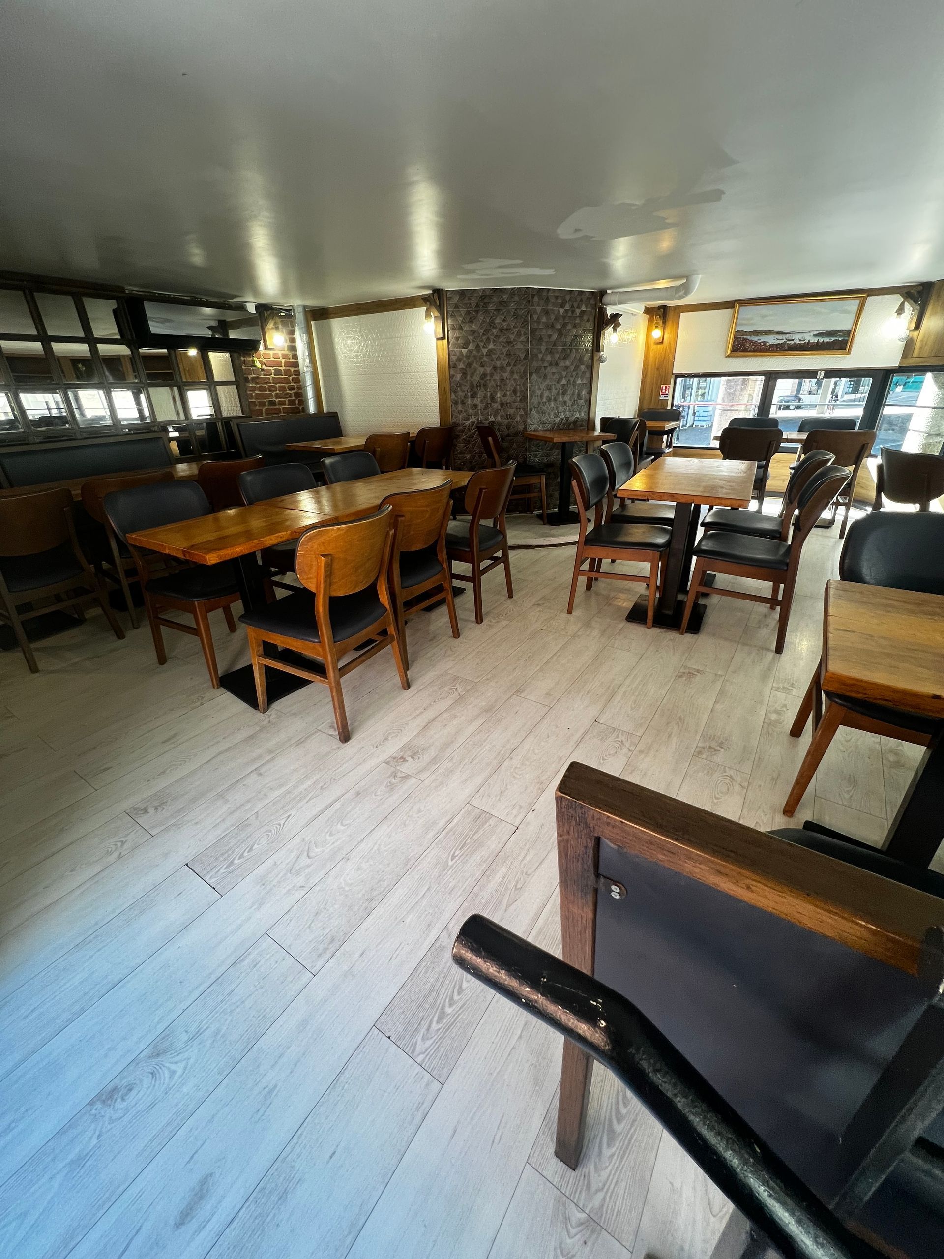 Vue intérieure d'une salle à manger avec des tables et des chaises en bois disposées sur un parquet clair.