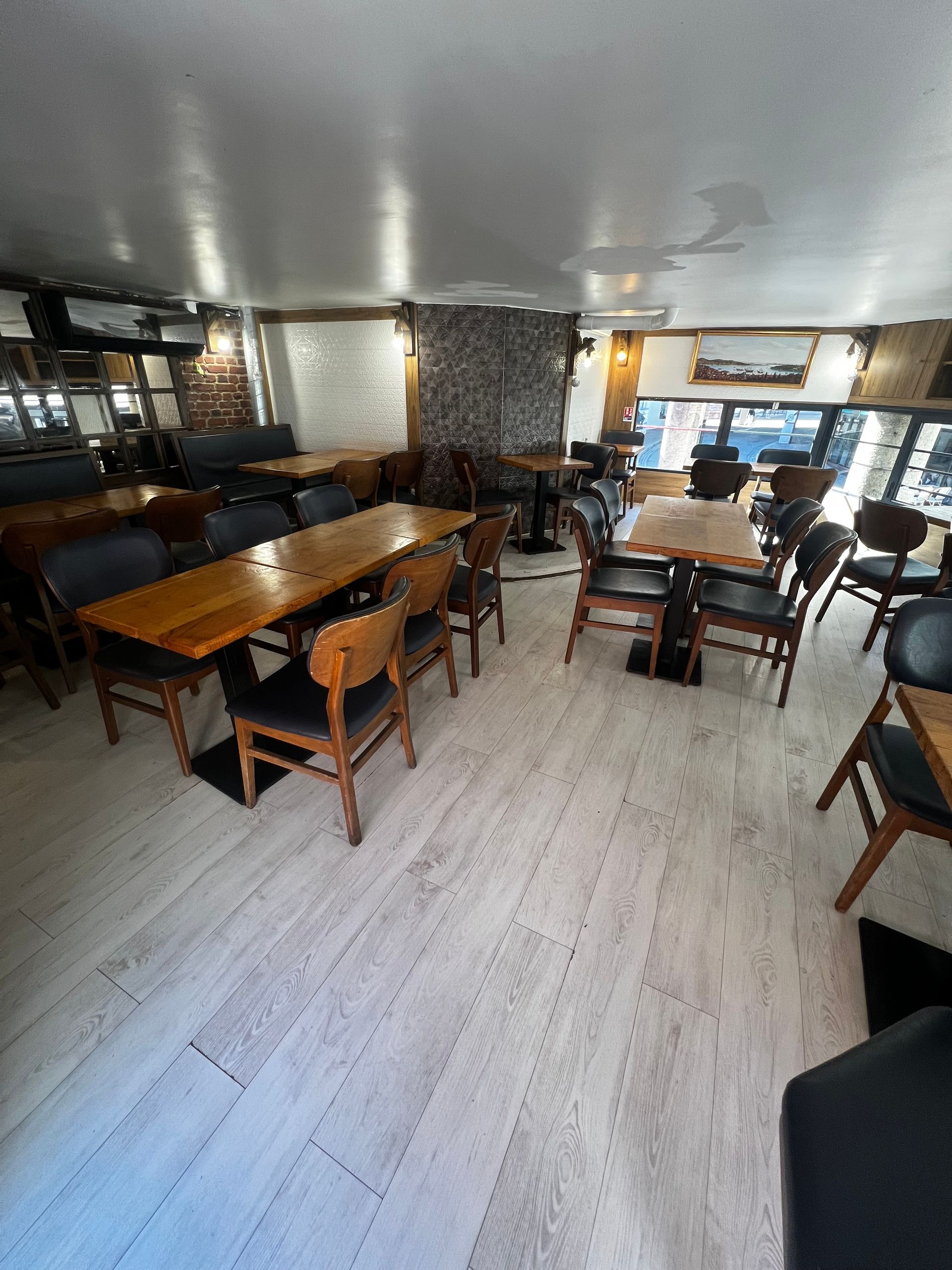 Vue intérieure d'un restaurant avec des rangées de tables en bois et des chaises noires sur un parquet clair.