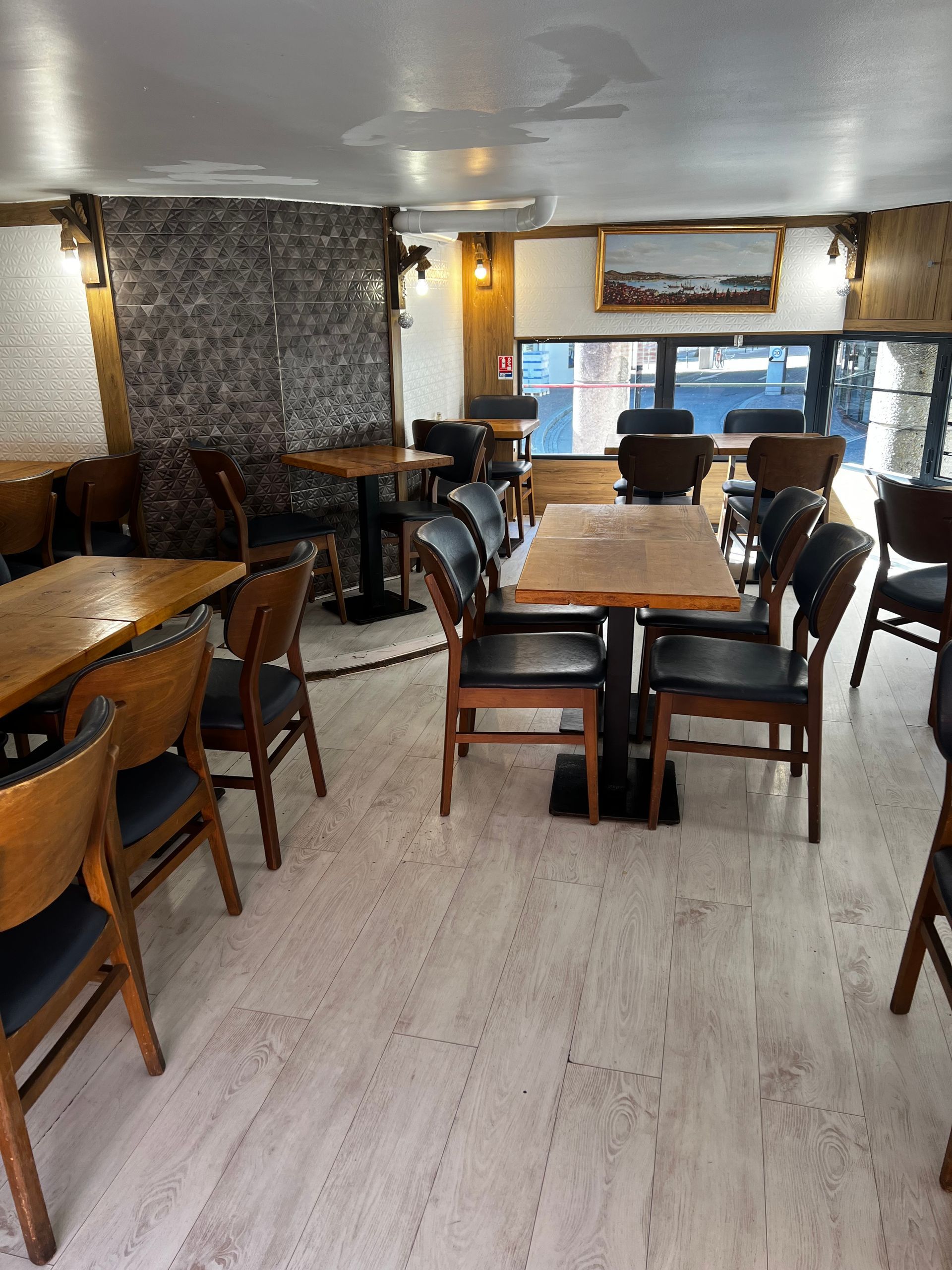 Intérieur d'un restaurant vide avec des tables en bois, des chaises noires et un parquet clair sous un éclairage chaleureux.