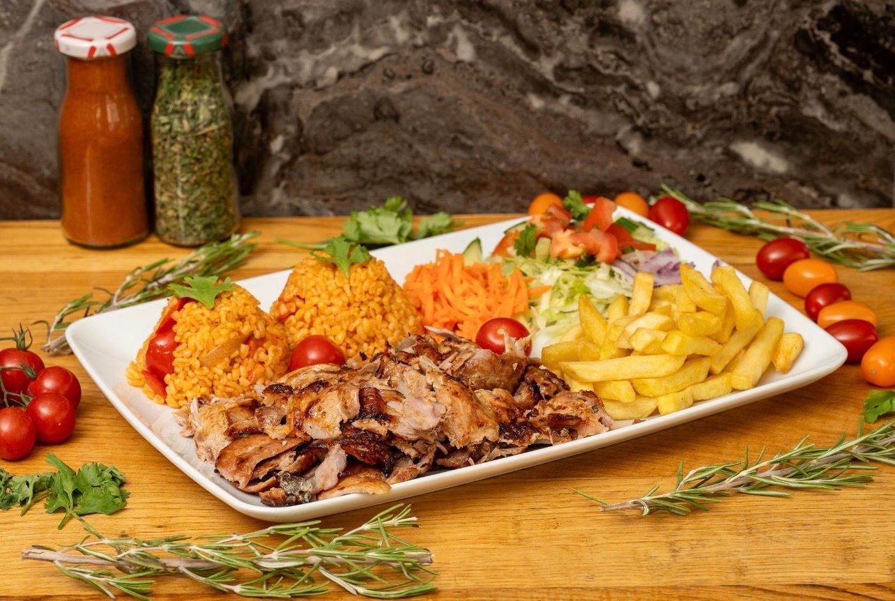 Une assiette blanche rectangulaire garnie de viande tranchée, de riz orange, de salade et de frites, posée sur une table en bois.