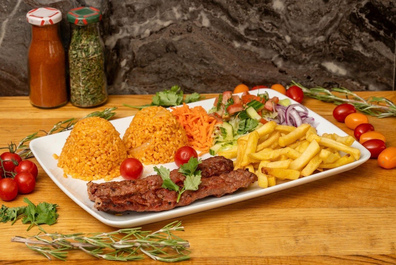 Une assiette de viande grillée, de riz jaune, de frites, de salade et de crudités servie sur une table en bois.