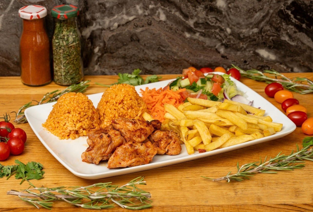 Une assiette rectangulaire blanche garnie de poulet grillé, de deux boules de riz à l'orange, de frites et d'une salade fraîche en accompagnement.