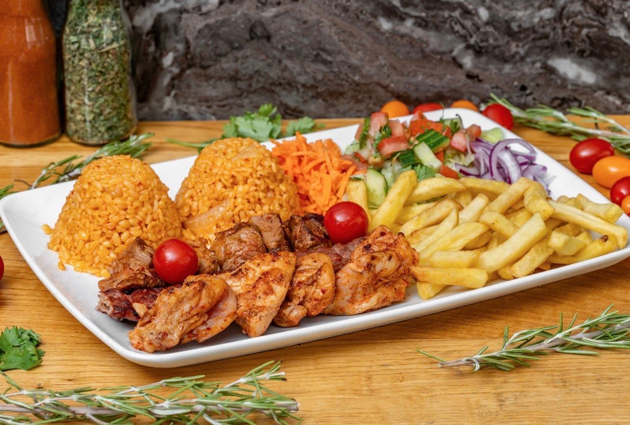 Une assiette rectangulaire garnie de poulet grillé, de deux boules de riz à l'orange, de frites, de carottes râpées et d'une salade fraîche en accompagnement.