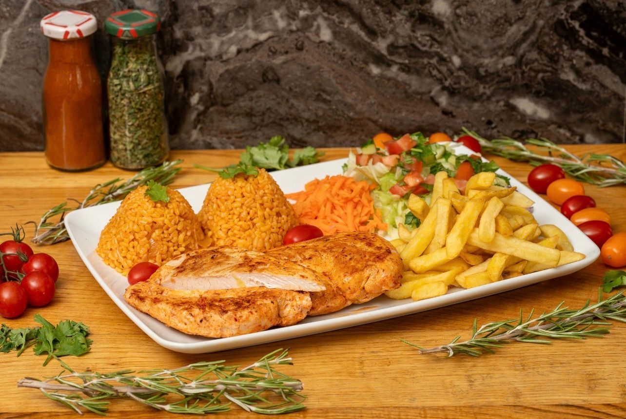 Une assiette de poulet grillé accompagnée de deux boules de riz à l'orange, de carottes râpées, de frites et d'une salade.