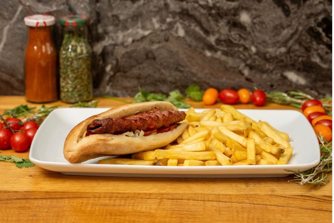 Une saucisse dans un petit pain fendu, servie avec une montagne de frites dorées sur une assiette rectangulaire blanche.