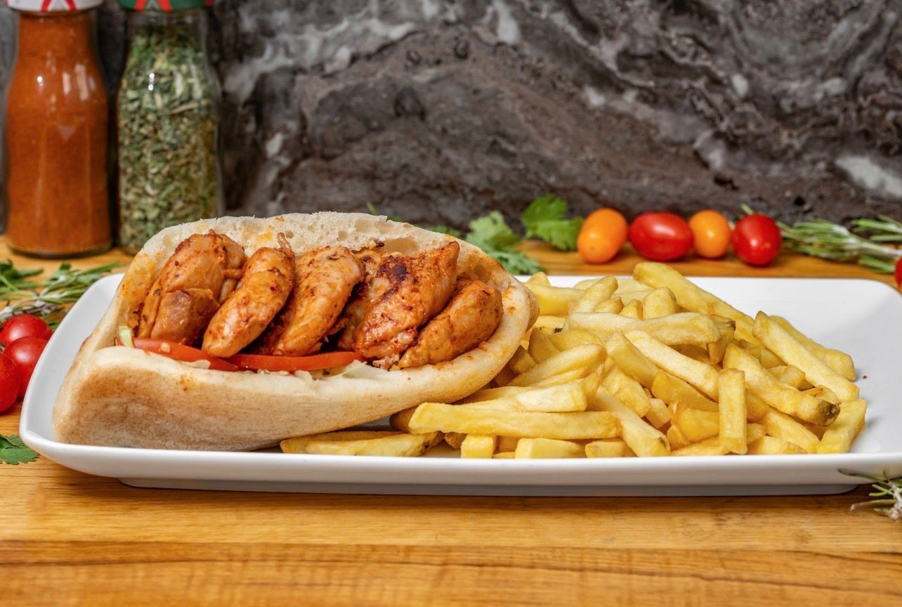 Un sandwich garni de tranches de poulet grillé et de tomate, servi avec des frites sur une assiette rectangulaire blanche.