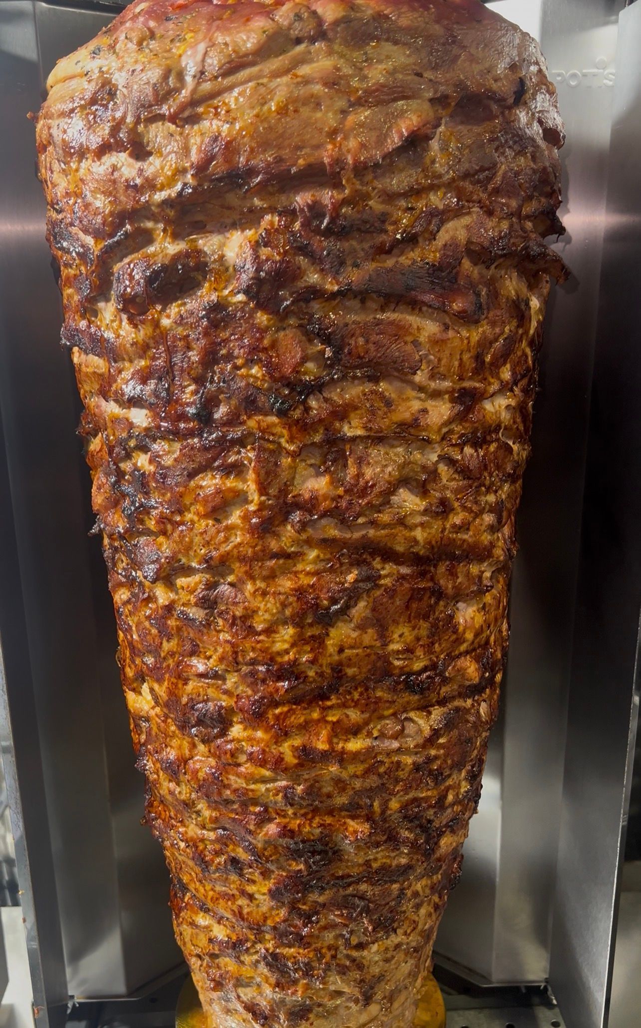 Un grand cône vertical de viande rôtie et assaisonnée, en train de cuire sur une broche.