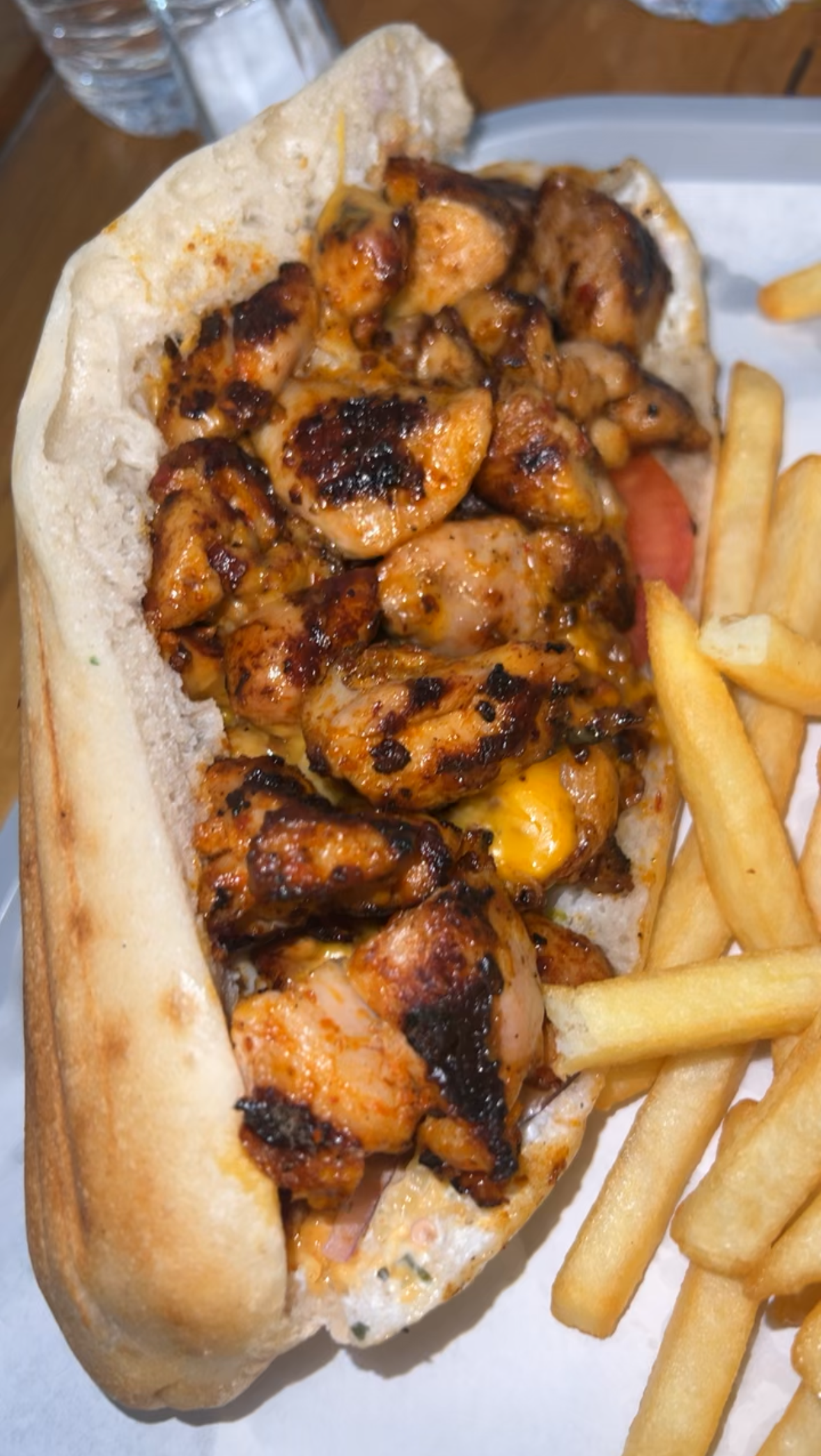 Un sandwich garni de morceaux de poulet grillés et assaisonnés et de fromage fondu, servi avec une portion de frites dorées.