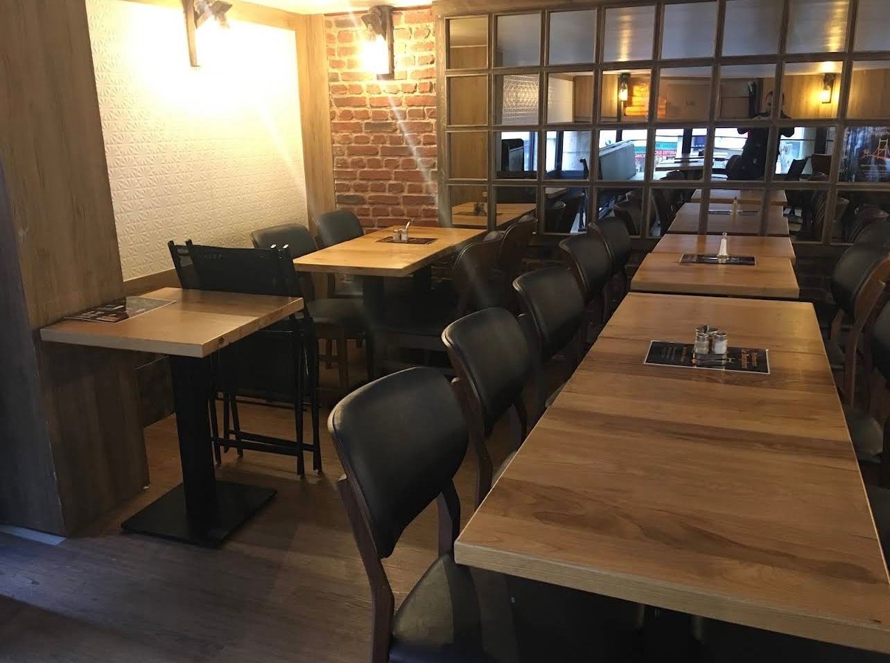 Une salle à manger intérieure avec des tables en bois clair, des chaises en cuir foncé et un mur en briques.