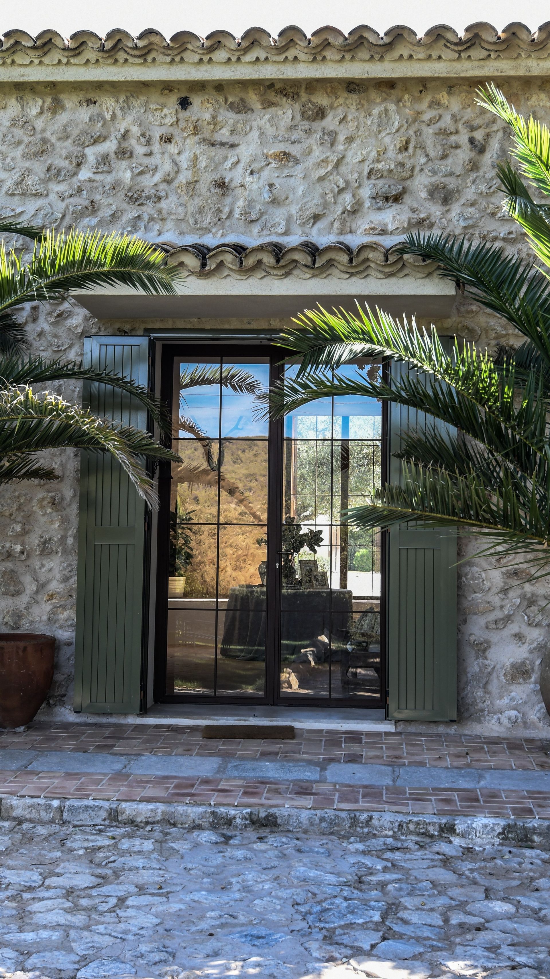 Un edificio de piedra con una puerta corrediza de vidrio y una palmera delante de él.