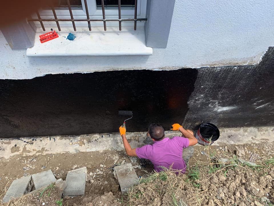 Un homme peint un mur extérieur en noir pour assurer l'isolation