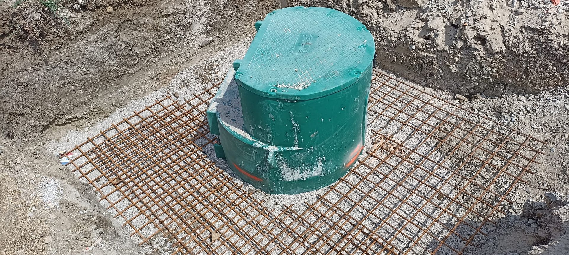 Un cylindre vert d'une borne d'assainissement dépasse d'un sol déblayé et quadrillé