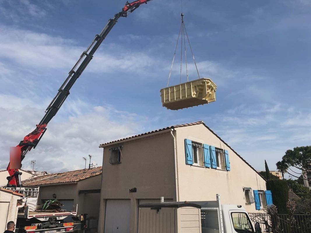 Une grue fait passer une piscine à coque au-dessus d'une maison