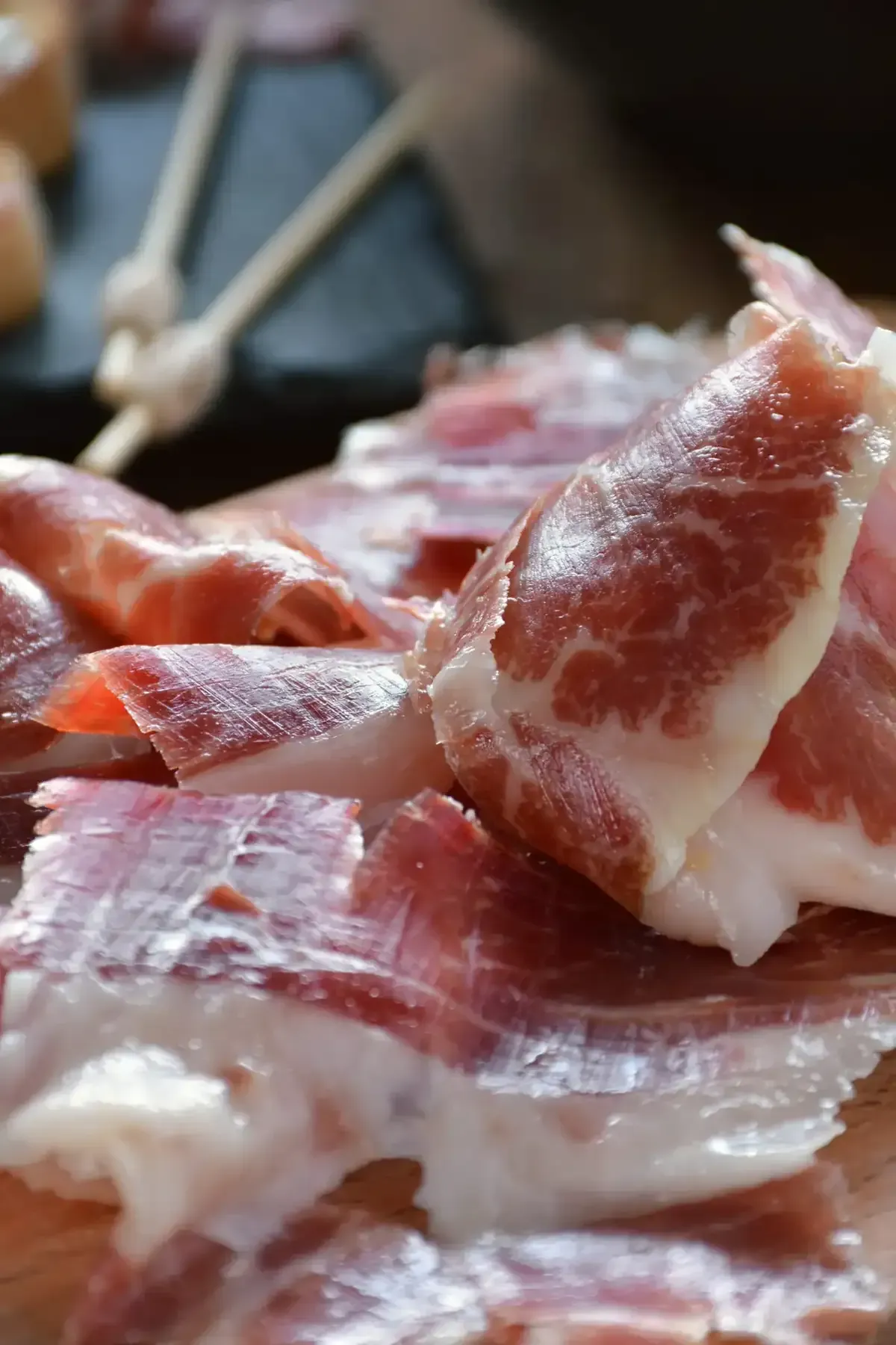 Finas lonchas veteadas de jamón curado, como el jamón ibérico, dispuestas sobre una superficie.