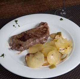 Un plato de filete sellado servido con patatas cocidas en rodajas sobre una superficie oscura.