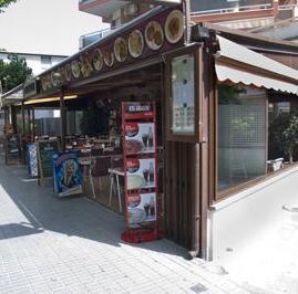 Vista de una esquina de la zona de comedor al aire libre de un restaurante, con un soporte para menús en la acera y una hilera de fotos de platos en la fachada.