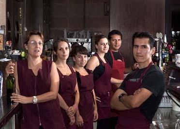 Un grupo de empleados de servicio con uniformes color granate haciendo fila dentro de un bar o restaurante.