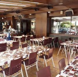 El interior de un restaurante con filas de mesas con manteles estampados, sillas marrones y techos de madera.