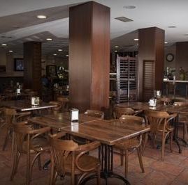 Un comedor de restaurante vacío con mesas de madera, sillas de madera curvada, suelo de baldosas y grandes pilares de soporte estructural.