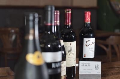 Varias botellas de vino, una de ellas con la etiqueta visible, reposan sobre una superficie de madera con una pequeña tarjeta informativa cerca.