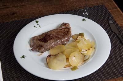 Un filete sellado a la plancha servido con patatas en rodajas en un plato blanco, colocado sobre un mantel individual oscuro.