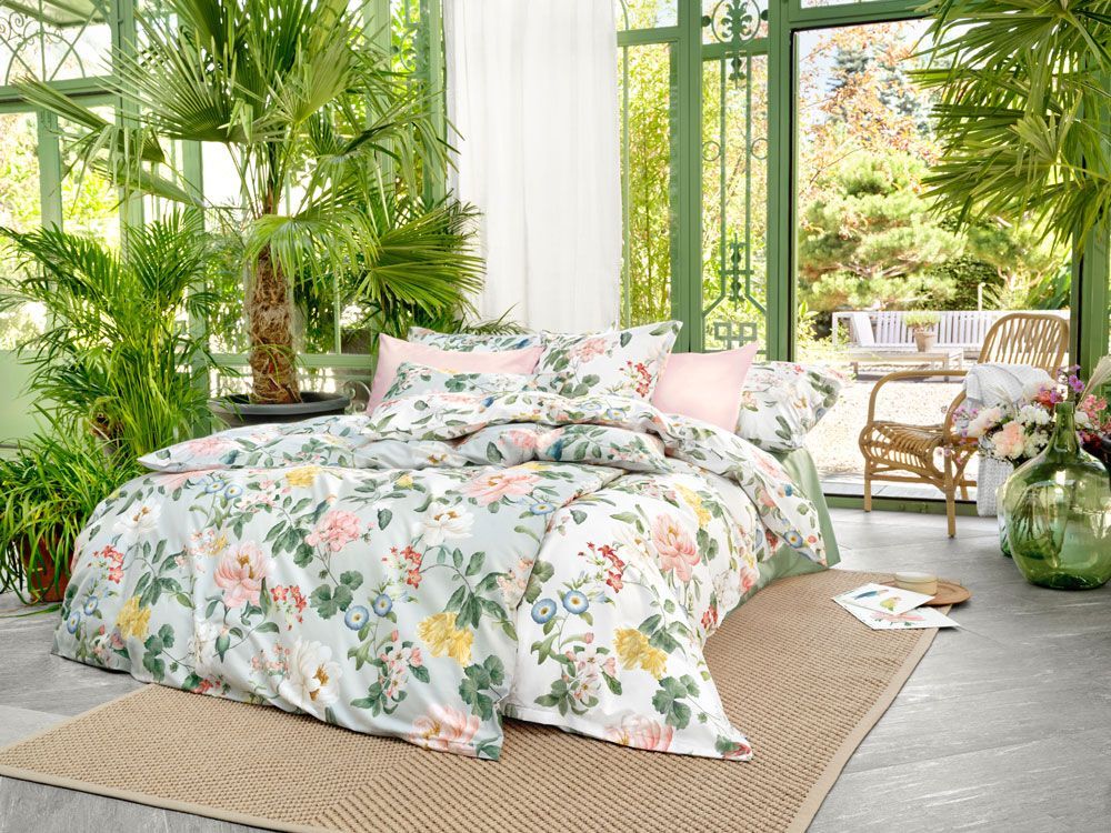 Ein Bett mit geblümter Bettdecke und Kissen in einem Gewächshaus.