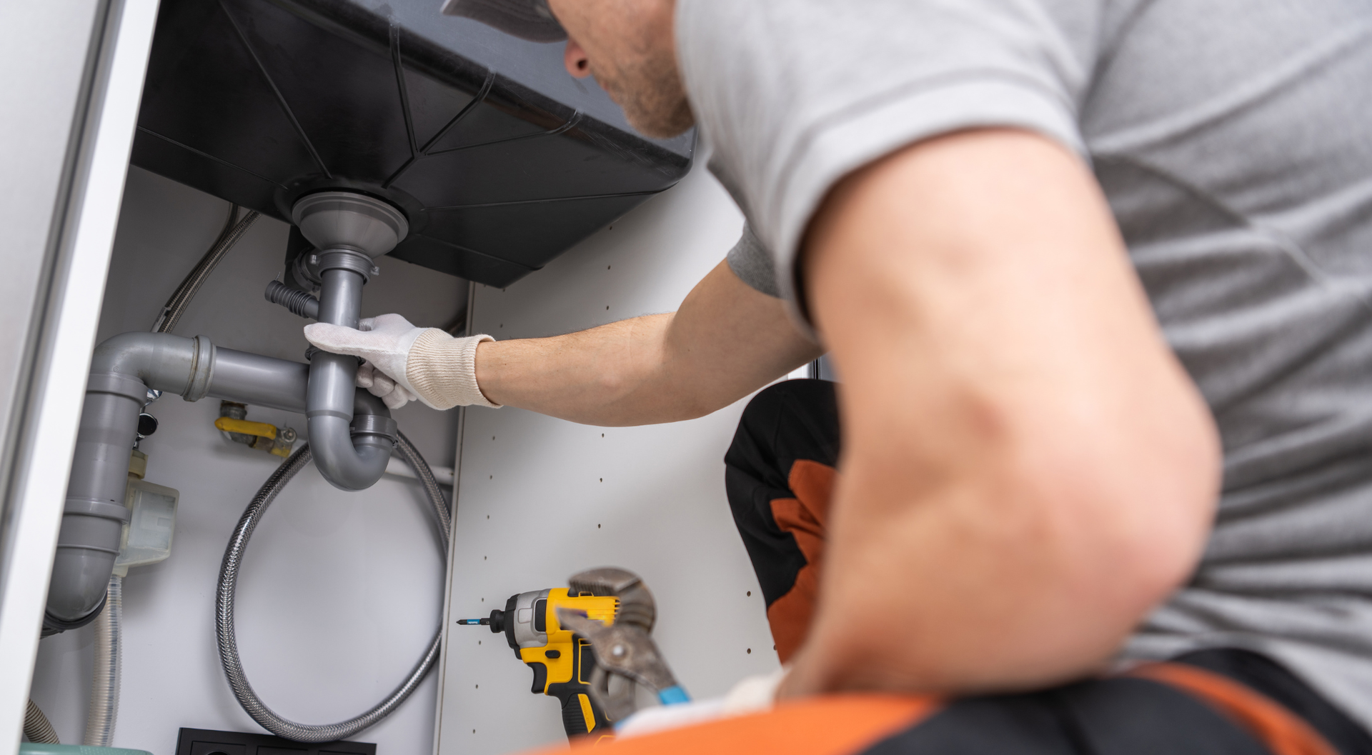 Fontanero debajo de un fregadero, trabajando en tuberías con un taladro.